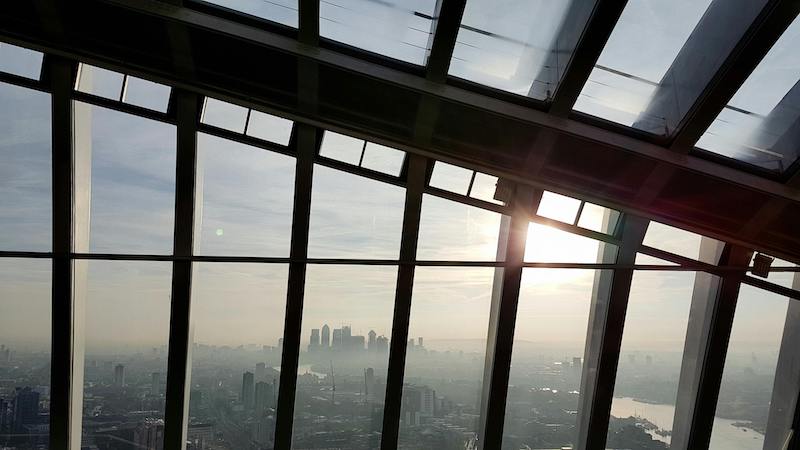 Golden hour sunlight illuminating a modern office interior with panoramic views of London, highlighting the city skyline and creating a warm, inviting atmosphere.